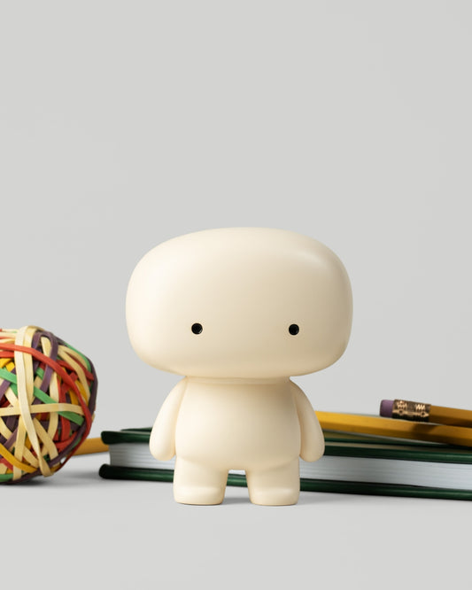 Blumo figure on a desk beside a rubber band ball, pencils, and notebooks