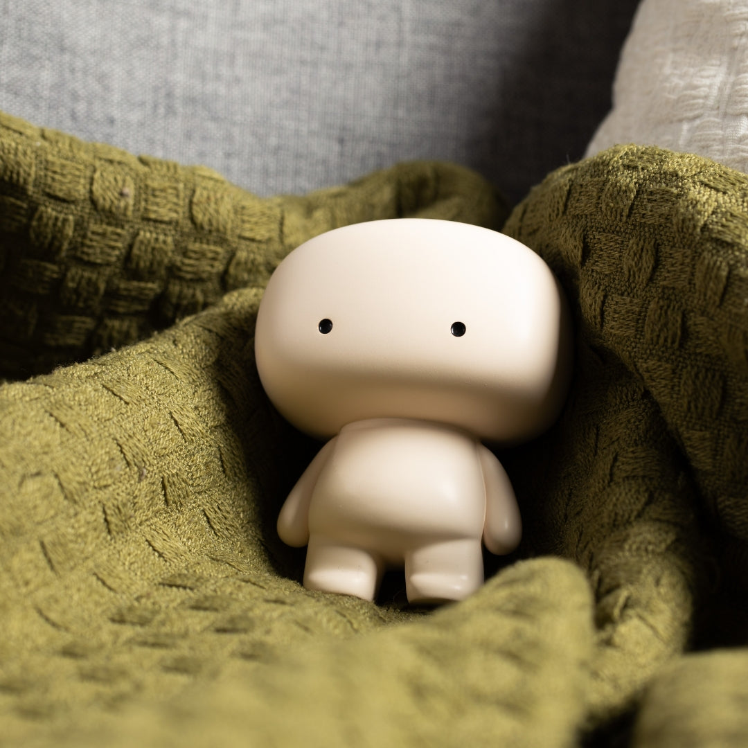 Blumo figure nestled in a folded olive green knit blanket