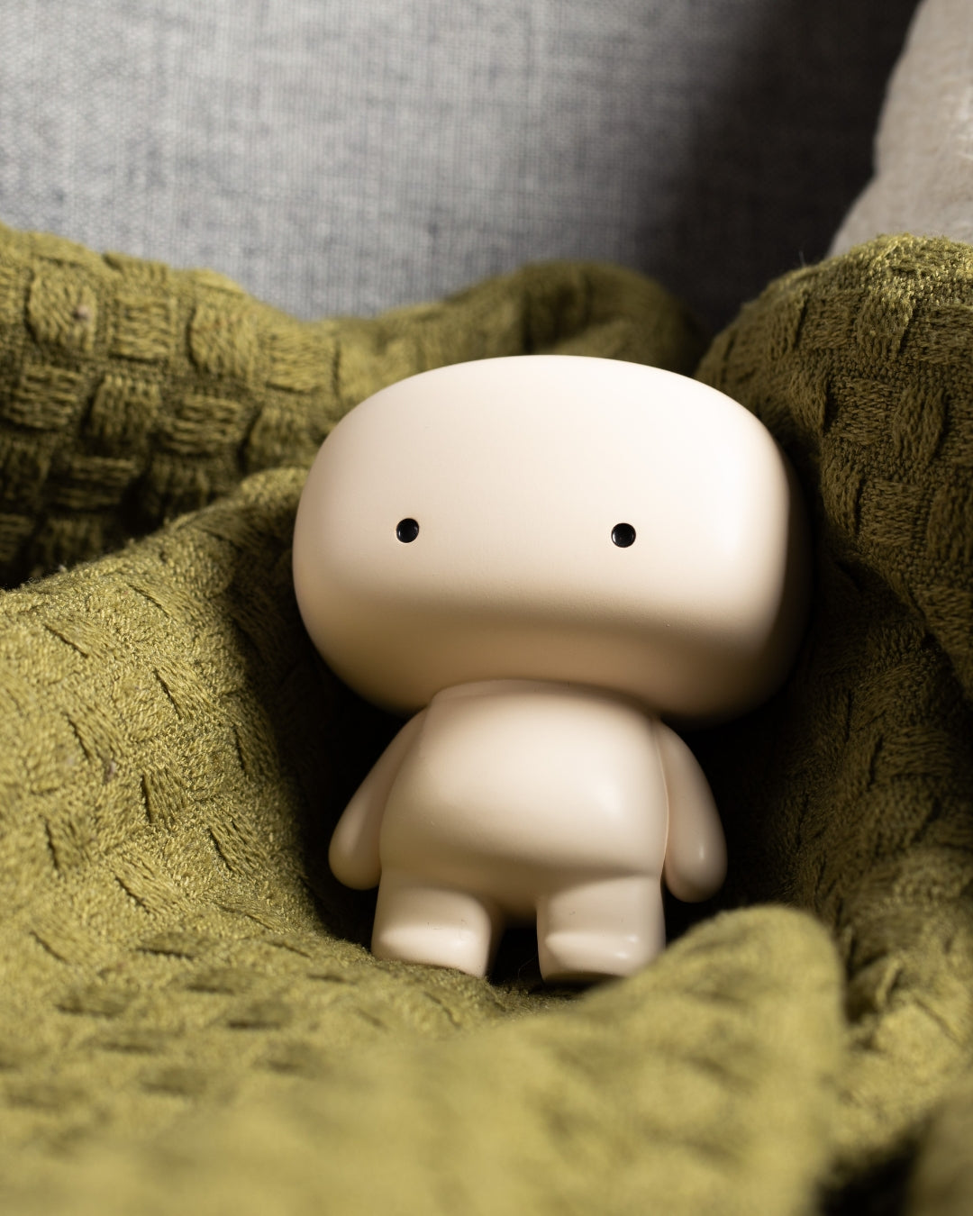 Blumo figure nestled in a folded olive green knit blanket