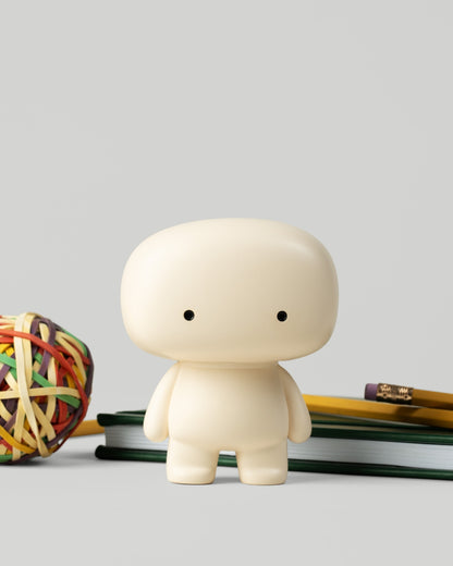 Blumo figure on a desk beside a rubber band ball, pencils, and notebooks